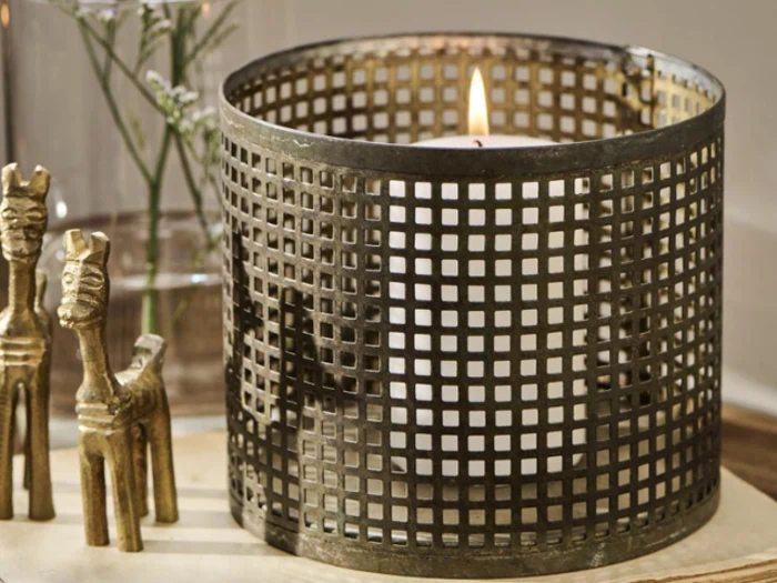 Et hvidt lys, der brænder i en metalgitterholder, med to små dekorative gulddyrfigurer ved siden af.