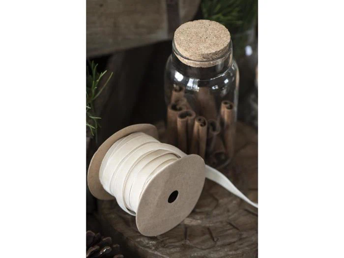 En glaskrukke fyldt med kanelstænger og forseglet med en kork sidder ved siden af en spole med hvidt bånd på et rustikt træbord.