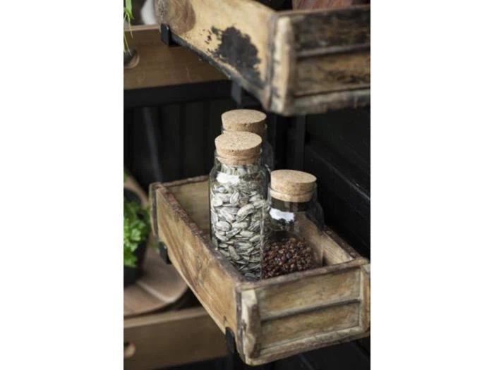 To glaskrukker med korklåg, den ene fyldt med solsikkefrø og den anden med peberkorn, står i en rustik træbakke på en hylde.