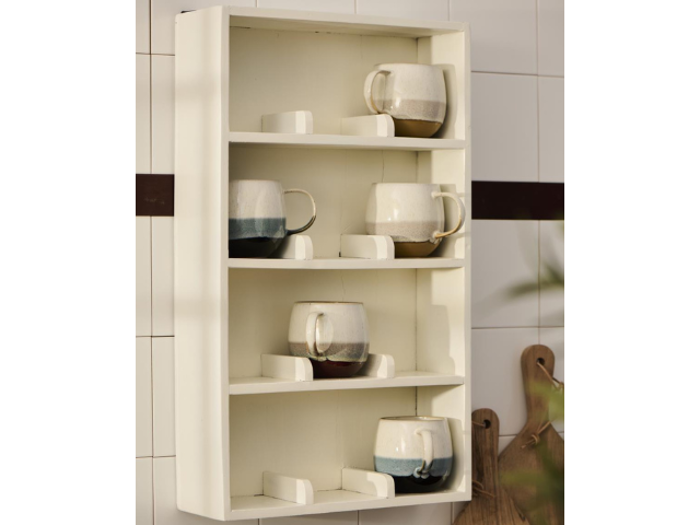 En hvid væghængt hylde med tre hylder, der hver rummer to eller tre keramikkrus i cremefarvede, brune og blå nuancer, udstillet i et køkken.