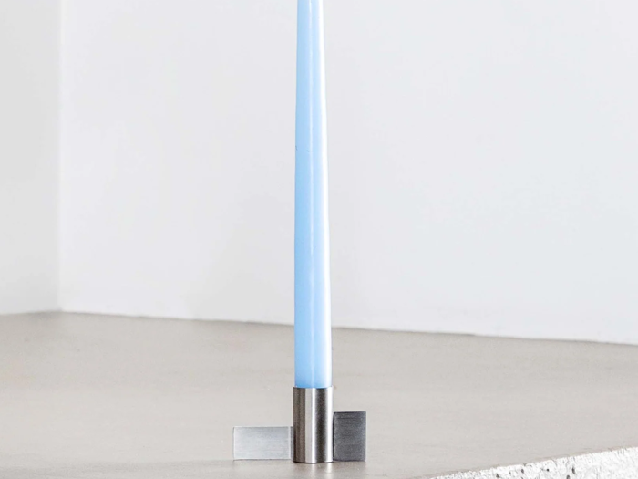 Et lyseblåt bloklys står i en minimalistisk sølvfarvet metalstage på en glat, lys overflade.