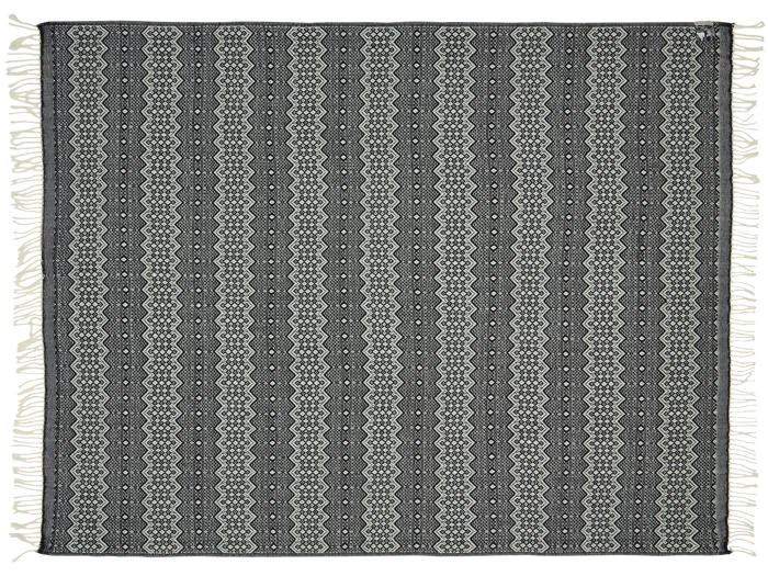 Rektangulært vævet tekstil med sorte og hvide lodrette zigzag- og diamantmønstre, frynsede kanter på alle sider, vist fladt mod en hvid baggrund.