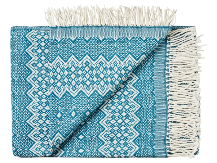 Et foldet blågrønt og hvidt vævet tæppe med geometriske mønstre og frynsede kanter, hvor det ene hjørne er vendt for at vise bagsiden.