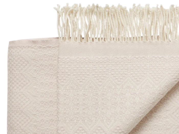 Et nærbillede af et foldet cremefarvet håndklæde med frynser og et diskret zigzagmønster.