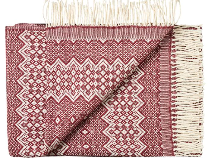 Et foldet rødt og hvidt mønstret vævet tæppe med frynsede kanter, der viser geometriske diamant- og zigzagmønstre.