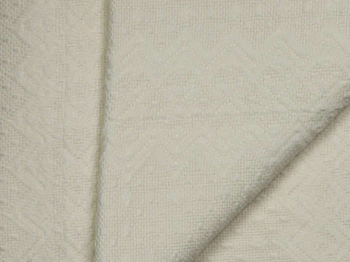Et nærbillede af foldet off-white struktureret stof med et subtilt zigzag- og diamantmønster vævet ind i materialet.