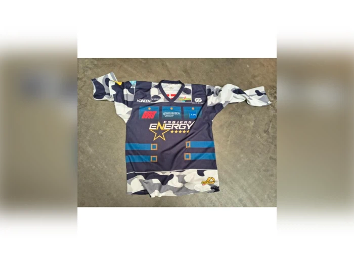 Blå og hvid sportstrøje i camouflagemønster med sponsorlogoer, et stjernemotiv og teksten Energy på forsiden, lagt fladt på en grå overflade.