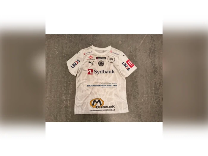 Hvid fodboldtrøje med forskellige sponsorlogoer, herunder Sydbank, på forsiden og ærmerne.