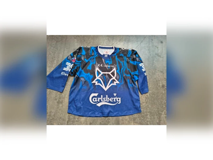 Blå hockeytrøje med et stiliseret rævelogo, Carlsberg-sponsortekst og forskellige andre logoer på en grå baggrund.