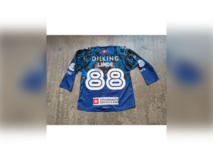 En blå ishockeystrøje med navnet DILLING LINDE og nummeret 88 på ryggen samt flere sponsorlogoer. Strøjen ligger fladt på et betongulv.