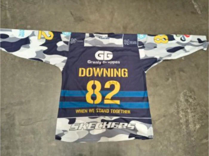 En sportstrøje i camouflagemønster med teksten DOWNING 82 og WHEN WE STAND TOGETHER på ryggen samt forskellige sponsorlogoer.