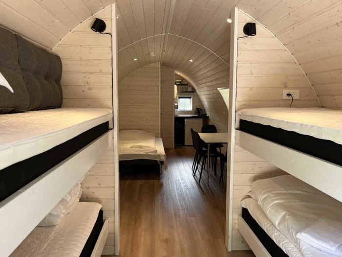 En hyggelig træhytte med to sæt køjesenge, en enkeltseng bagerst og et lille køkken og spiseplads i den anden ende.