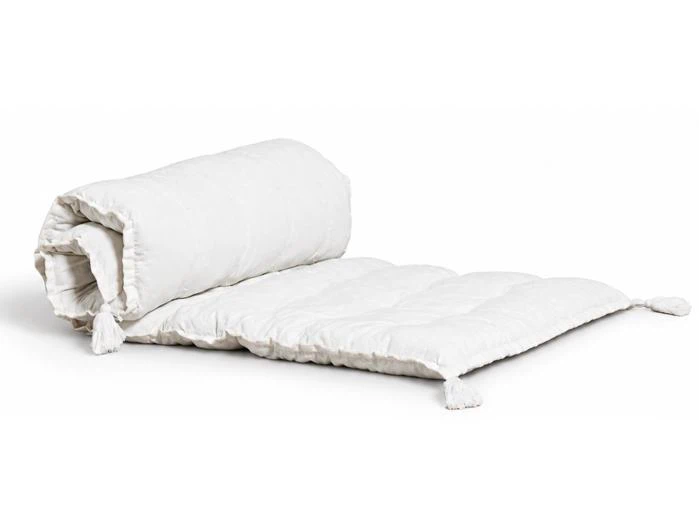 En off-white, quiltet gulvmåtte, der er delvist rullet sammen, med kvaster i hjørnerne.