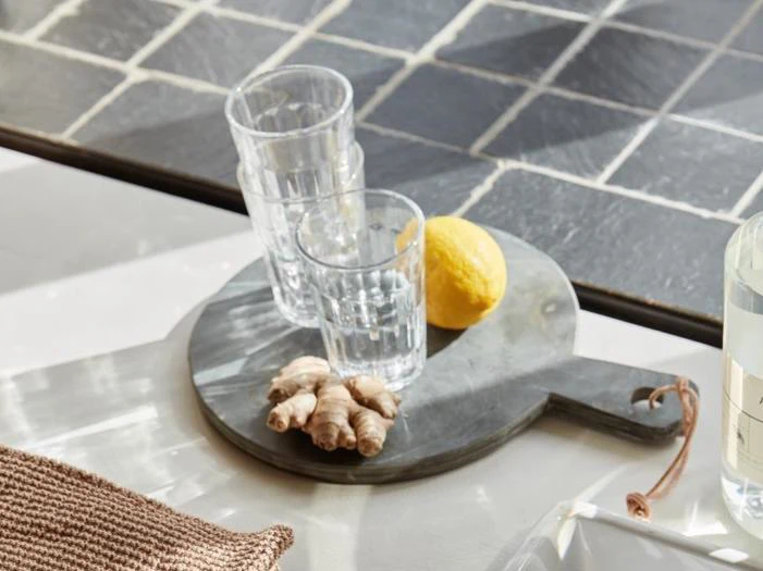 To glas stablet oven på hinanden, en citron og et stykke ingefær på et lille, mørkt, rundt serveringsbræt.