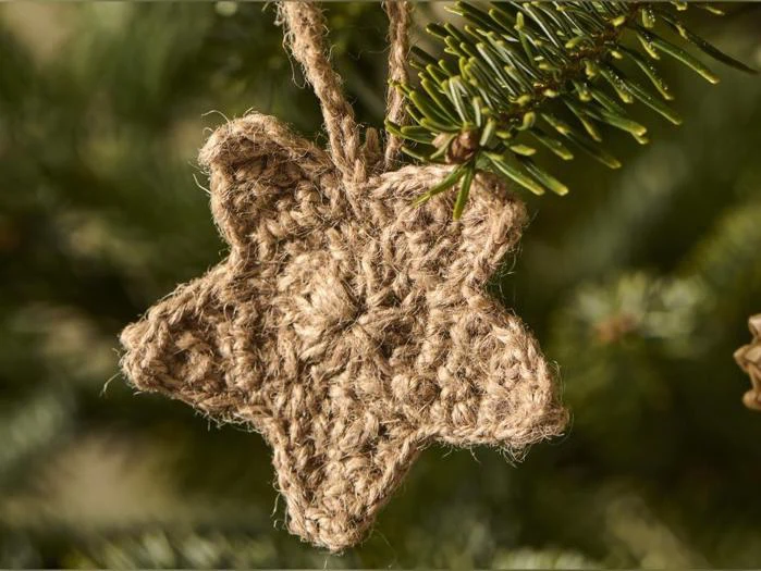 En hæklet stjernepynt lavet af brunt garn, der hænger på en gren på juletræet.