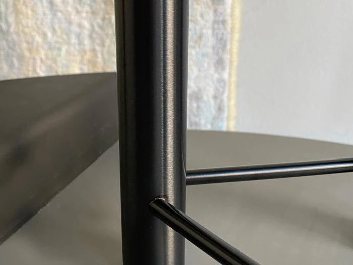 Et nærbillede af et bordben af sort metal og dets bærende ramme.