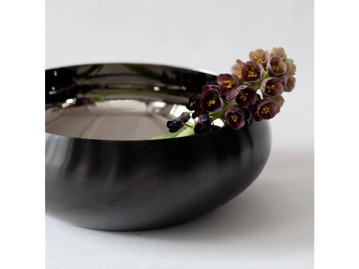 En sort skål med en lille buket mørkviolette, klokkeformede blomster.