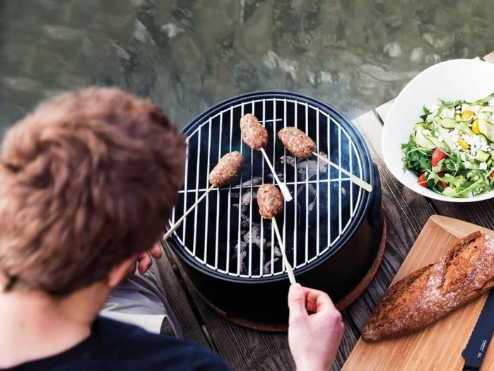 En person, der griller fire kødspyd på en lille kulgrill ved siden af en salat og et brød.
