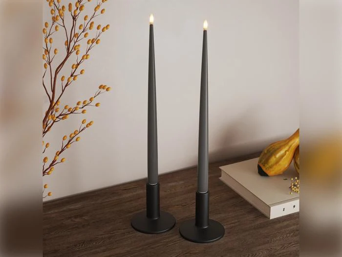 To høje, sorte, tilspidsede stearinlys med flammer på en træoverflade, ved siden af en gul kalabas, en lukket bog og en gren med små gule bær.