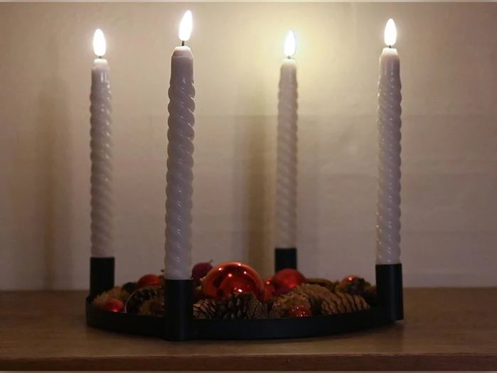 En adventskrans med fire tændte, spiralformede hvide stearinlys, pyntet med fyrrekogler og røde pynteting.