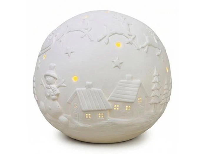 Hvid, kugleformet keramisk lampe med et præget motiv af en vinterlandsby med huse, en snemand og træer, der er oplyst indefra.