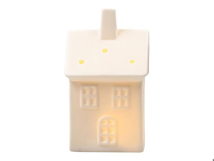 Hvid keramisk lampe i form af et hus med lysende vinduer og en skorsten.