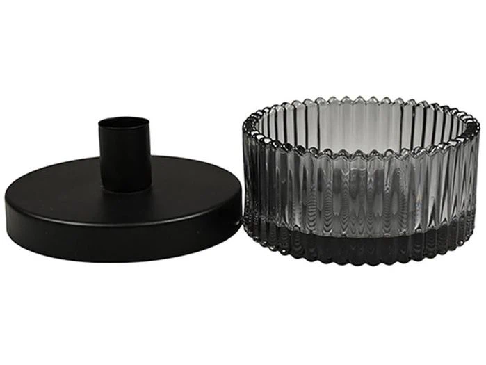 Et rundt, sort metal låg med et håndtag i midten ved siden af en cirkulær, riflet krukke af klart glas.