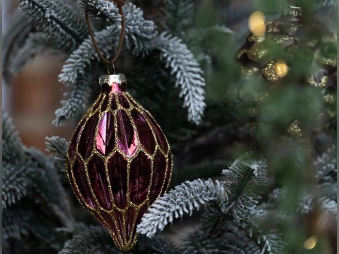Et facetteret, dybrødt julepynt med guldglitterdetaljer, der hænger på en flokket stedsegrøn gren.