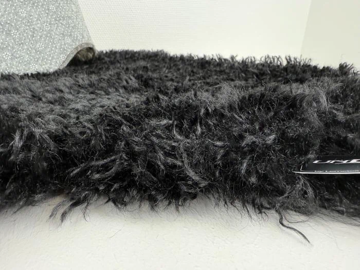 Et nærbillede af et sort, loddent stof med et lille, synligt mærke til højre og en sølvfarvet, glitrende genstand i baggrunden.