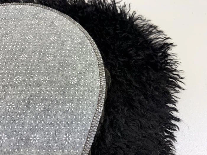 Et nærbillede af et gråt, blomstermønstret stof med syede kanter, der ligger på en lodden, sort overflade.