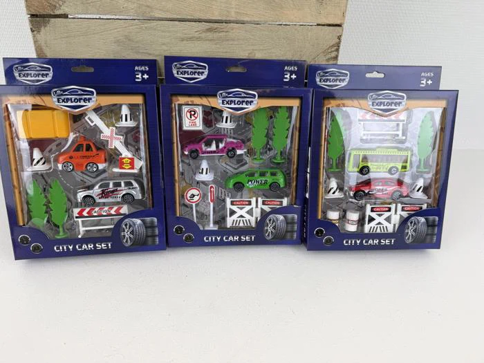 Tre sæt med legetøjsbiler i æsker til børn fra 3 år, som hver indeholder legetøjsbiler, vejskilte, træer og tilbehør, der står oprejst på en træbaggrund.