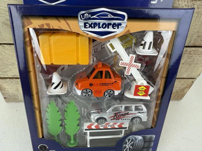 Legetøjssæt i emballage mærket Little Explorer med en orange bil, en sølvfarvet politibil, træer, trafikkegler, vejskilte og en gul klods.