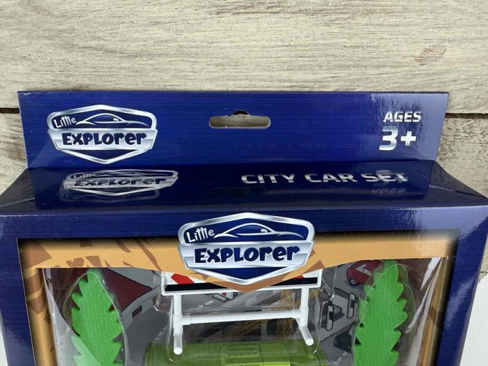 Nærbillede af en legetøjspakke mærket Little Explorer City Car Set med en blå æske og en tekst, hvor der står Ages 3+. En del af legetøjet indeni er synligt.