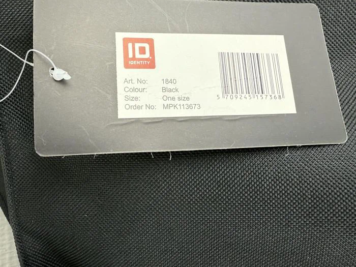 Et tøjmærke på en sort stofvare viser en stregkode og detaljer: Art. nr: 1840, Farve: Sort, Størrelse: One size, Order No: MPK113673, og brand ID Identity.