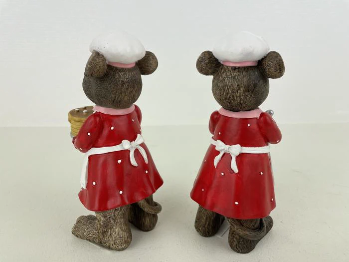 To bjørnefigurer i røde kjoler og hvide kokkehuer står ryg mod ryg; den ene holder en kurv, den anden holder et køkkenredskab.