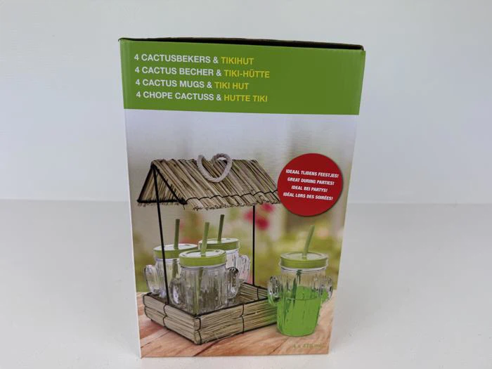 En æske med et sæt på fire kaktusformede krus med låg og sugerør i en lille tiki-hytte-holder af træ.