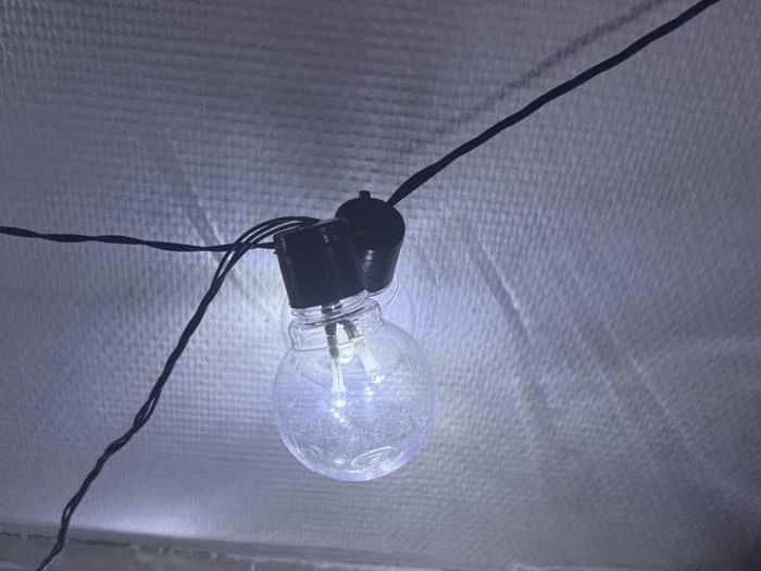 En glødende lyspære hænger på en sort ledning mod en struktureret, hvid baggrund.