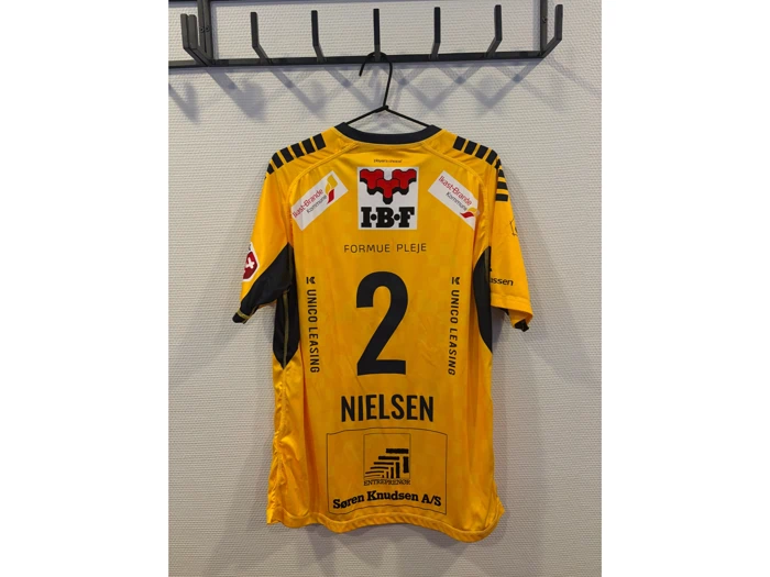 En gul sportstrøje med nummer 2 og navnet »Nielsen« på ryggen, der hænger på en krog. Trøjen er prydet med forskellige sponsorlogoer.