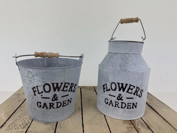 To metalbeholdere med træhåndtag mærket FLOWERS & GARDEN står på en træplade; den ene er en spand, og den anden er en dunk.