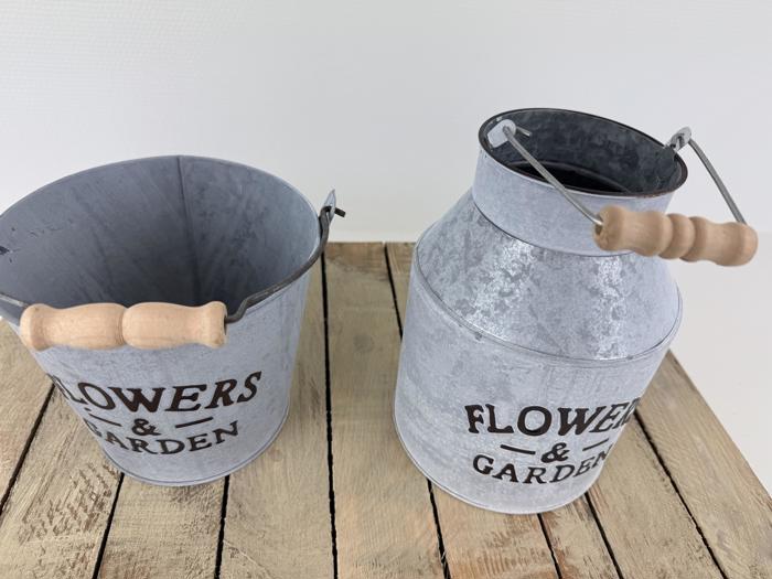 To metalbeholdere med træhåndtag mærket FLOWERS & GARDEN står på en træoverflade; den ene er en spand, den anden er en kande.