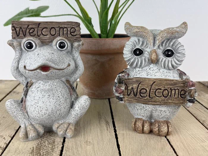 To stenfigurer, en frø og en ugle, der hver især holder et velkomstskilt i træ, sidder på en træplade med en potteplante i baggrunden.