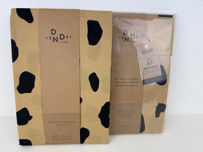 To Dindi Home-produkter med brun og sort plettet emballage, det ene pakket ind i brunt papir, det andet i klar plast med et REMO-mærke på.