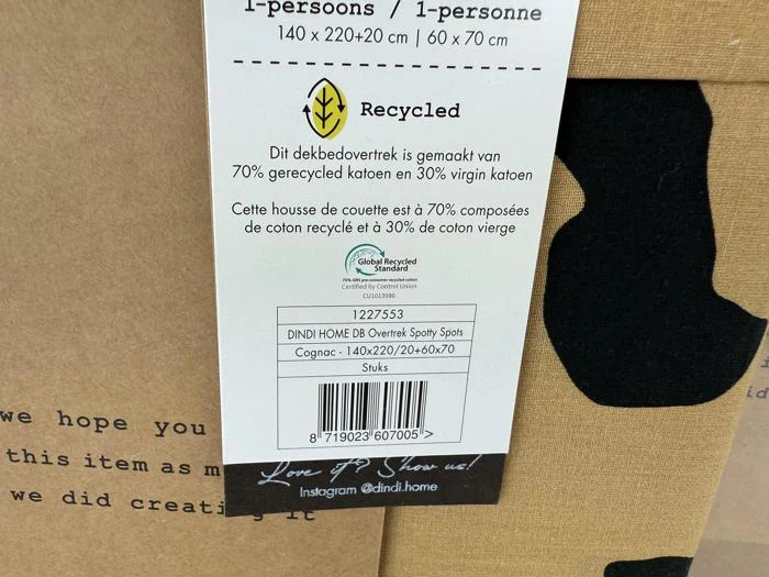 Et produktmærke til et dynebetræk af genanvendt bomuld med oplysninger om varen, mål og certificeringslogoer på hollandsk, fransk og engelsk.