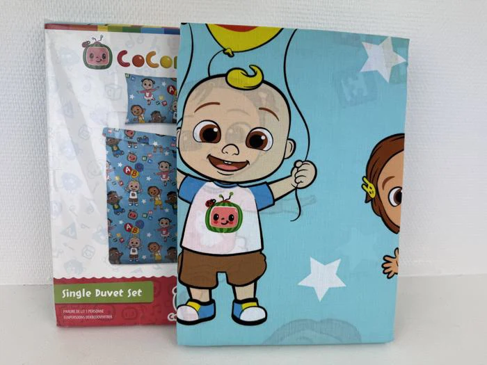 Et foldet CoComelon enkeltdyne-sæt med en smilende tegneserie-baby, der holder en ballon, og emballagen viser det samme design i baggrunden.