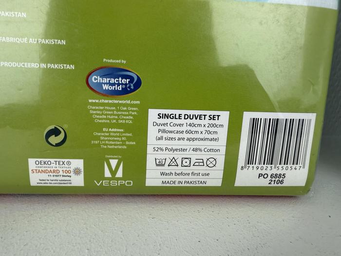 En produktetiket til et enkelt dynesæt, der viser størrelsesoplysninger, materialesammensætning, plejeanvisninger og oprindelse som Pakistan.