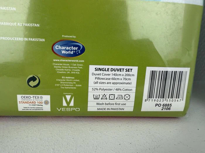 En produktetiket til et enkelt dynesæt, der viser størrelsesoplysninger, materialesammensætning, plejeanvisninger og oprindelse som Pakistan.