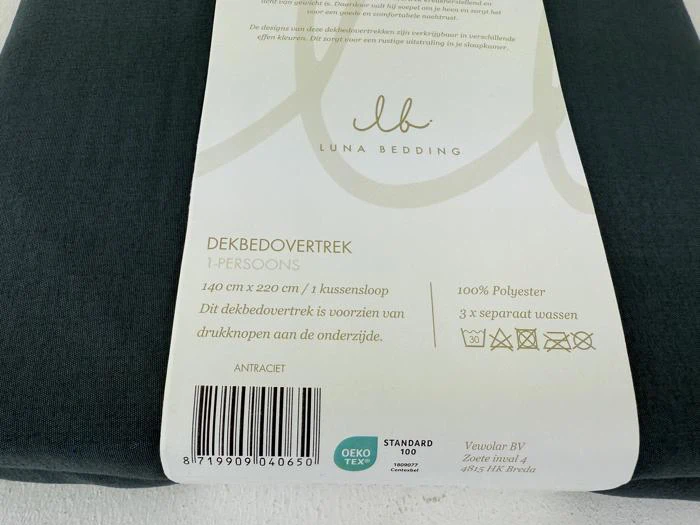Nærbillede af en Luna Bedding-pakke med et enkelt dynebetræk, der viser produktoplysninger, vaskeanvisninger og etiketter på en mørk stofbaggrund.