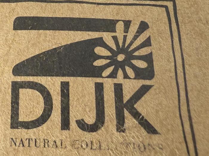 En sort grafik af et jern med en blomsterdetalje over den fede tekst DIJK på brunt tekstureret papir, med delvis tekst NATURAL COLLE... nedenunder.