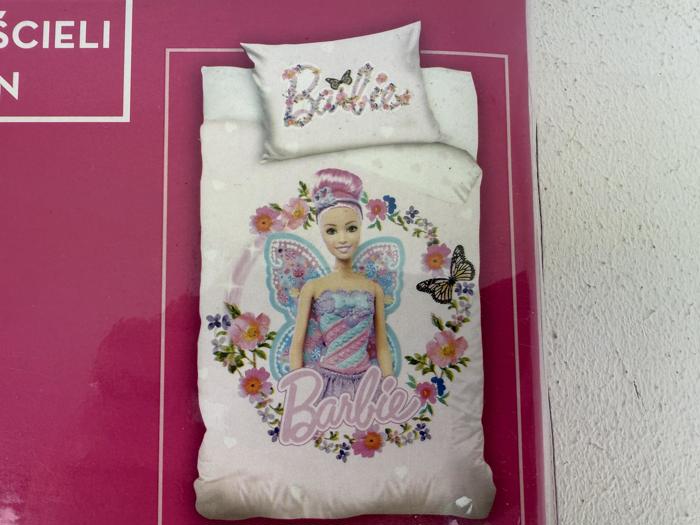 Et sengesæt med Barbie-tema med en eventyrlig Barbie med vinger, omgivet af blomster og sommerfugle, på en lyserød baggrund med ordet Barbie skrevet på dynen og puden.
