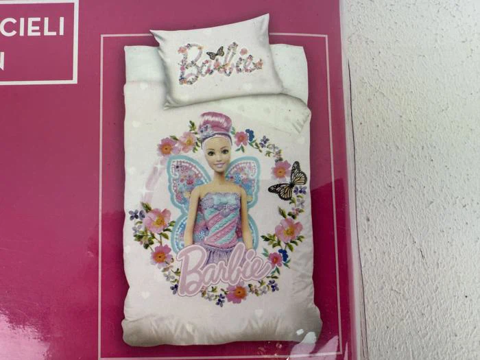 Et sæt med dynebetræk og pudebetræk i Barbie-fe-design med pink og lilla farver, blomster, en sommerfugl og ordet Barbie i dekorativ skrift.